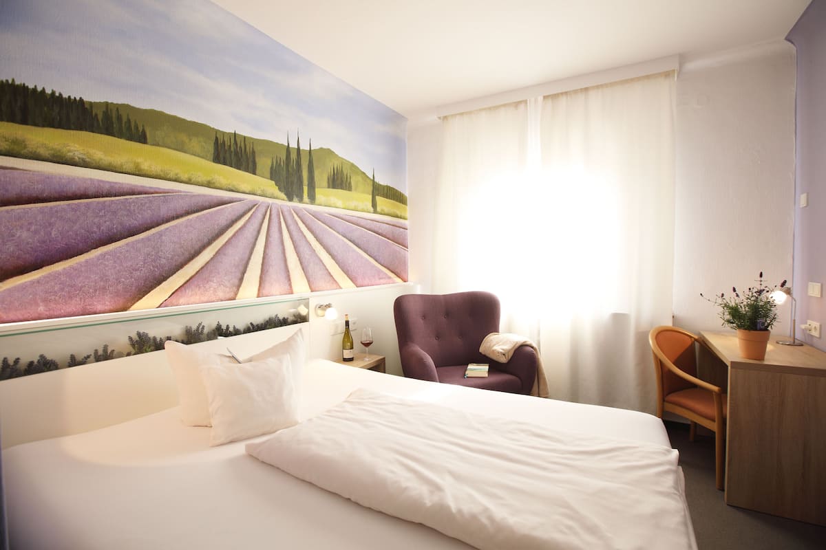 Habitación de hotel con cama, una silla, un escritorio y un gran mural de un viñedo.