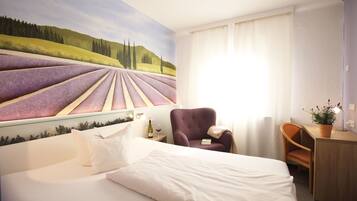 A hotel room with a bed, a chair, a desk, and a large mural of a vineyard.