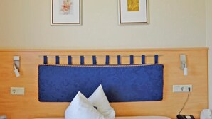 A hotel room with a wooden headboard, two framed artworks on the wall, a blue bedspread, and a white pillow.
