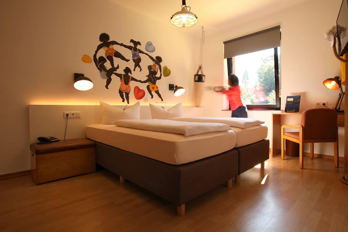 Un dormitorio con cama, mesita de noche, lámpara y un adorno en la pared.