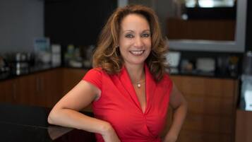 A woman in a red dress sitting at a kitchen counter with wooden cabinets and a black countertop.