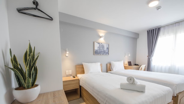 A hotel room with two beds, a potted plant, a wall-mounted light, and a painting. - COMMON INN Thao Dien (Ho Chi Minh City)