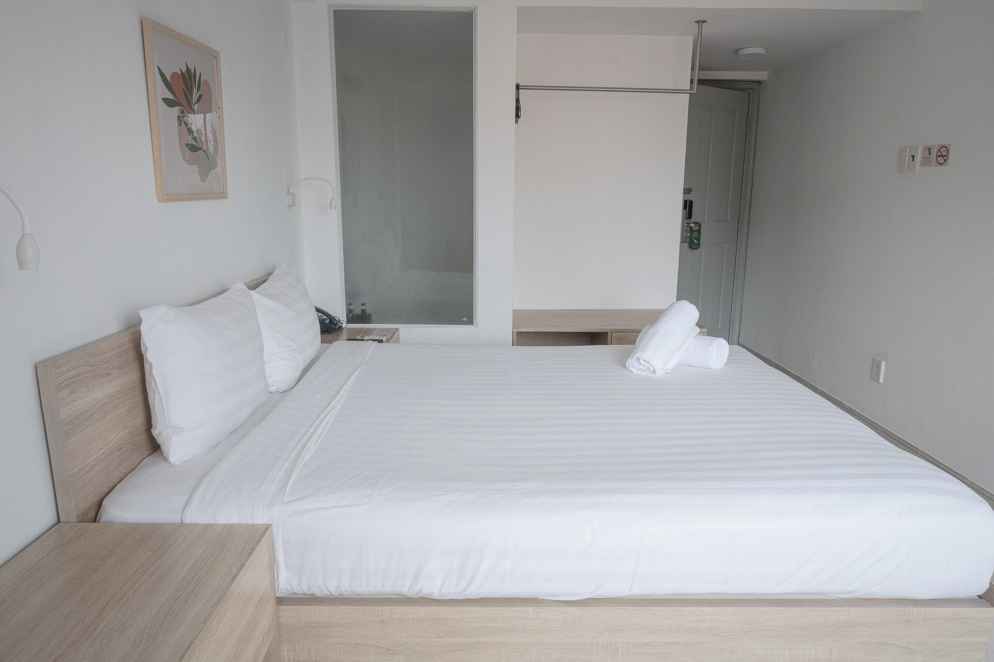 A neatly made bed with white linens, a wooden headboard, and a white nightstand.