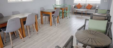 A spacious room with a dining area, seating arrangements, and large windows providing natural light.