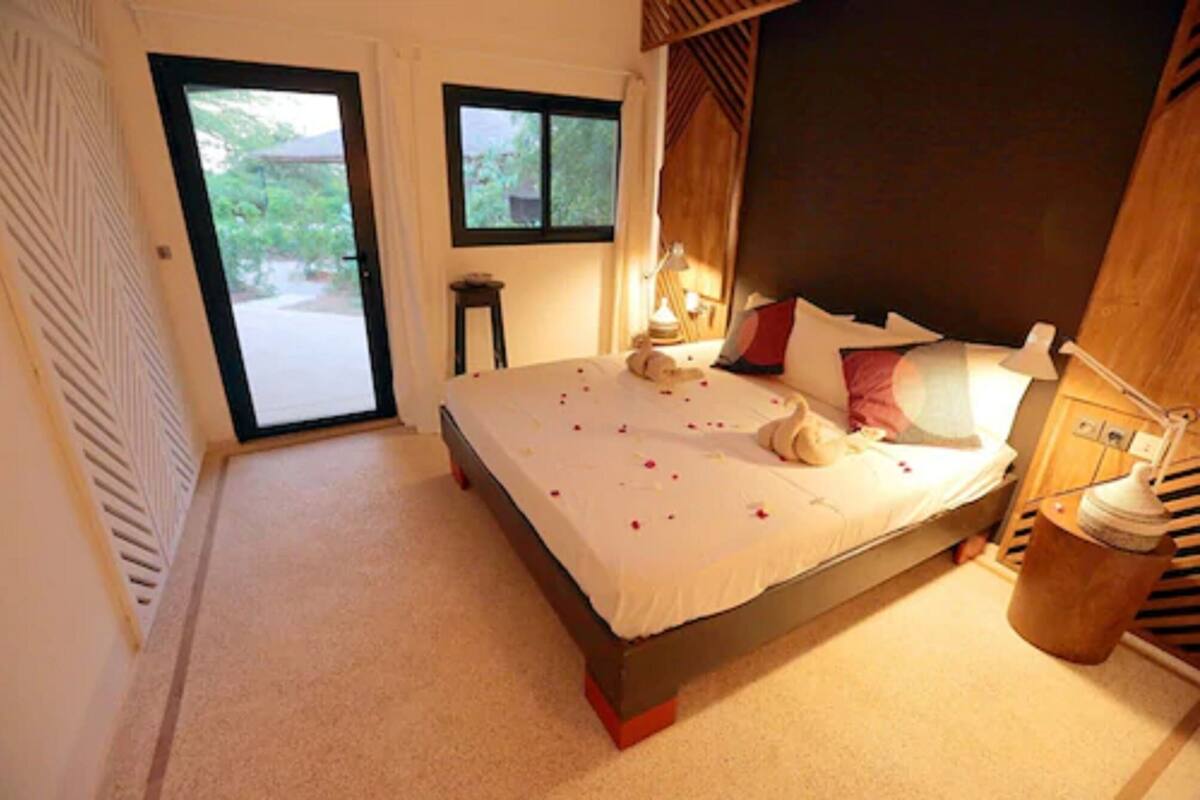 A bedroom with a bed, a nightstand, a lamp, and a window.