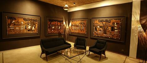 A modern interior with a glass coffee table, black sofas, and large framed artworks on the walls.