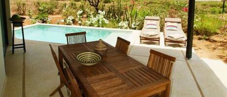 An outdoor dining area with a pool, wooden furniture, and a view of the landscape.