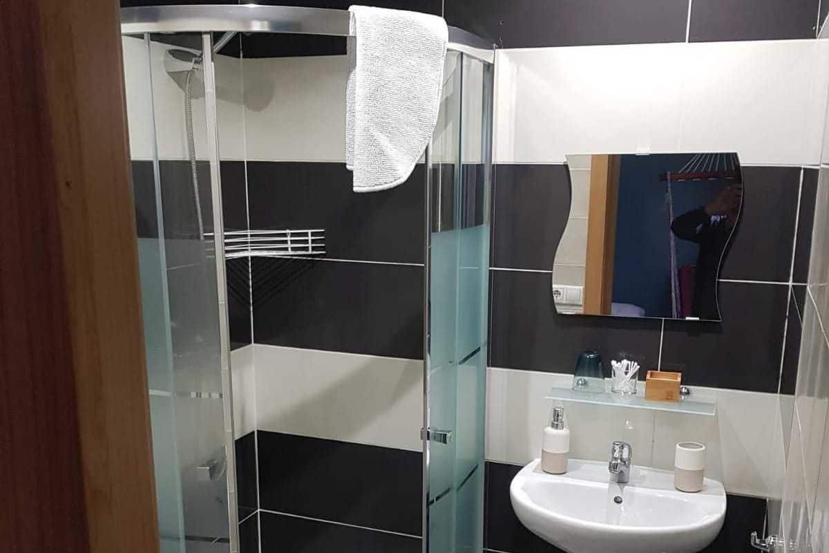 A modern bathroom with a glass-enclosed shower, a white sink, and a tiled floor.