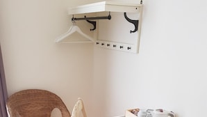 Una habitación con una silla de mimbre, un escritorio blanco con cafetera y un perchero en la pared.