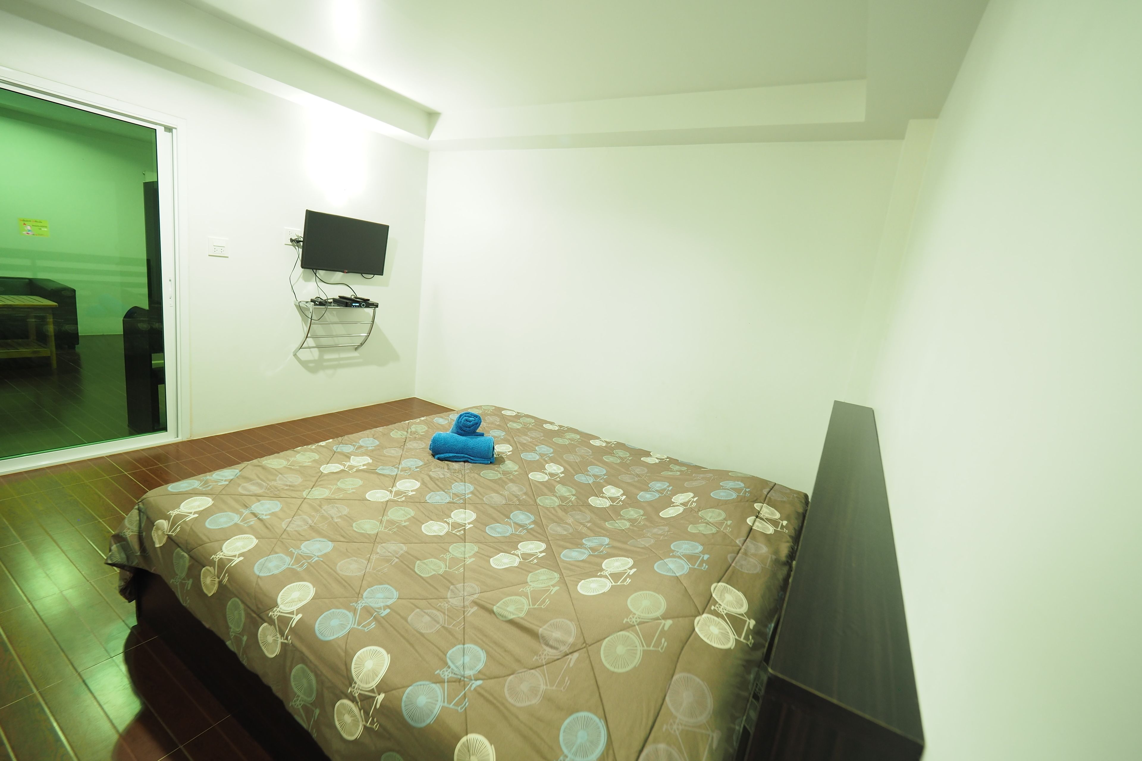 A bedroom with a bed, a TV mounted on the wall, and a sliding door leading to another room.