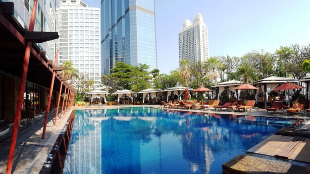 A swimming pool with lounge chairs and umbrellas, surrounded by trees and buildings.