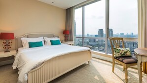 A hotel room with a large bed, two bedside tables, a chair, and a view of the cityscape through large windows.