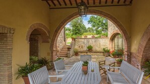An outdoor patio with a round table and white chairs, surrounded by brick arches and potted plants. - Agriturismo Cerreto (Pienza)