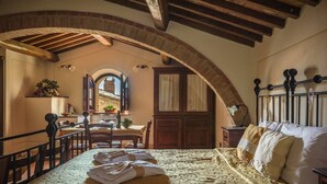 A cozy room with a bed, a wooden table, and a chair. There is a window with a view of a building outside. - Agriturismo Cerreto (Pienza)