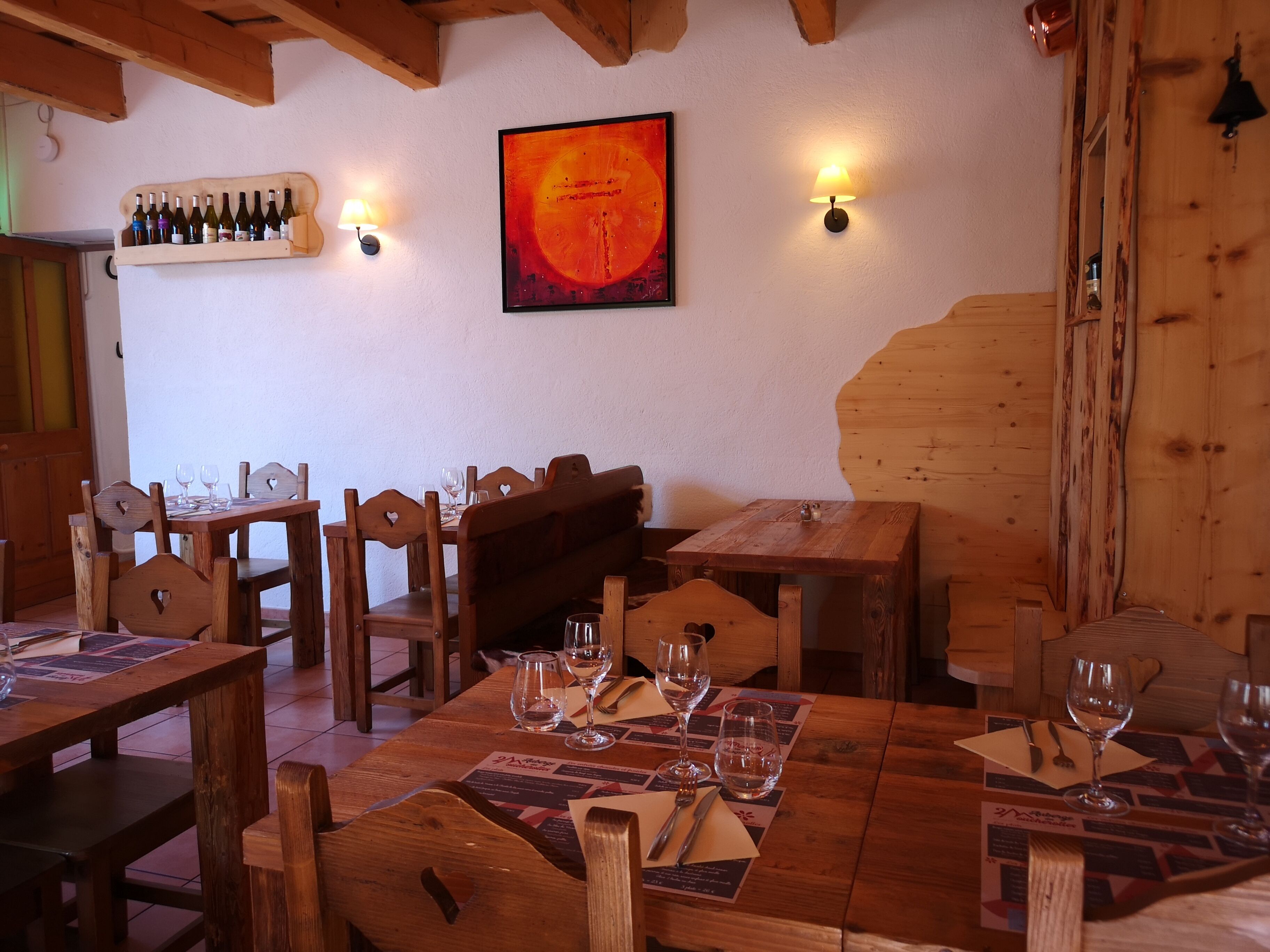 A rustic wooden dining area with tables and benches, a wall-mounted wine rack, and two wall sconces.