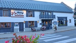 A two-story building with a sign reading "Auberge des Oucherolles" and a restaurant sign. There are outdoor seating areas with tables and chairs. - Auberge Les 2 Moucherolles (Correncon-en-Vercors)