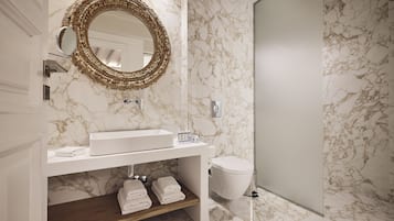 Un baño con pared de mármol, un lavabo con espejo y un inodoro.