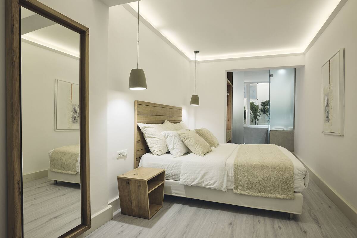 A modern bedroom with a wooden headboard, a bedside table, and a large mirror.