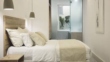Une chambre à coucher avec une tête de lit en bois, un lit avec une literie blanche, une table de chevet et des lampes suspendues.
