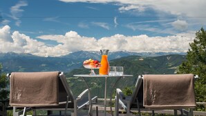 A table with a fruit bowl, a glass of orange juice, and two glasses, set against a mountain backdrop. - Gasthof Kohlern (Bolzano)