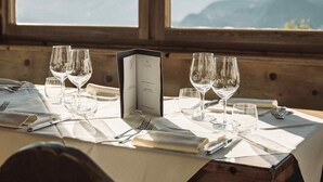 A dining table set with wine glasses and a menu, overlooking a mountainous landscape through a large window. - Gasthof Kohlern (Bolzano)