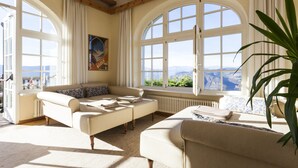 A spacious living room with a large arched window offering a mountain view, a sofa set, and a potted plant. - Gasthof Kohlern (Bolzano)