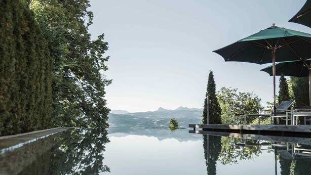 A serene infinity pool reflecting trees and a distant mountain range. - Gasthof Kohlern (Bolzano)