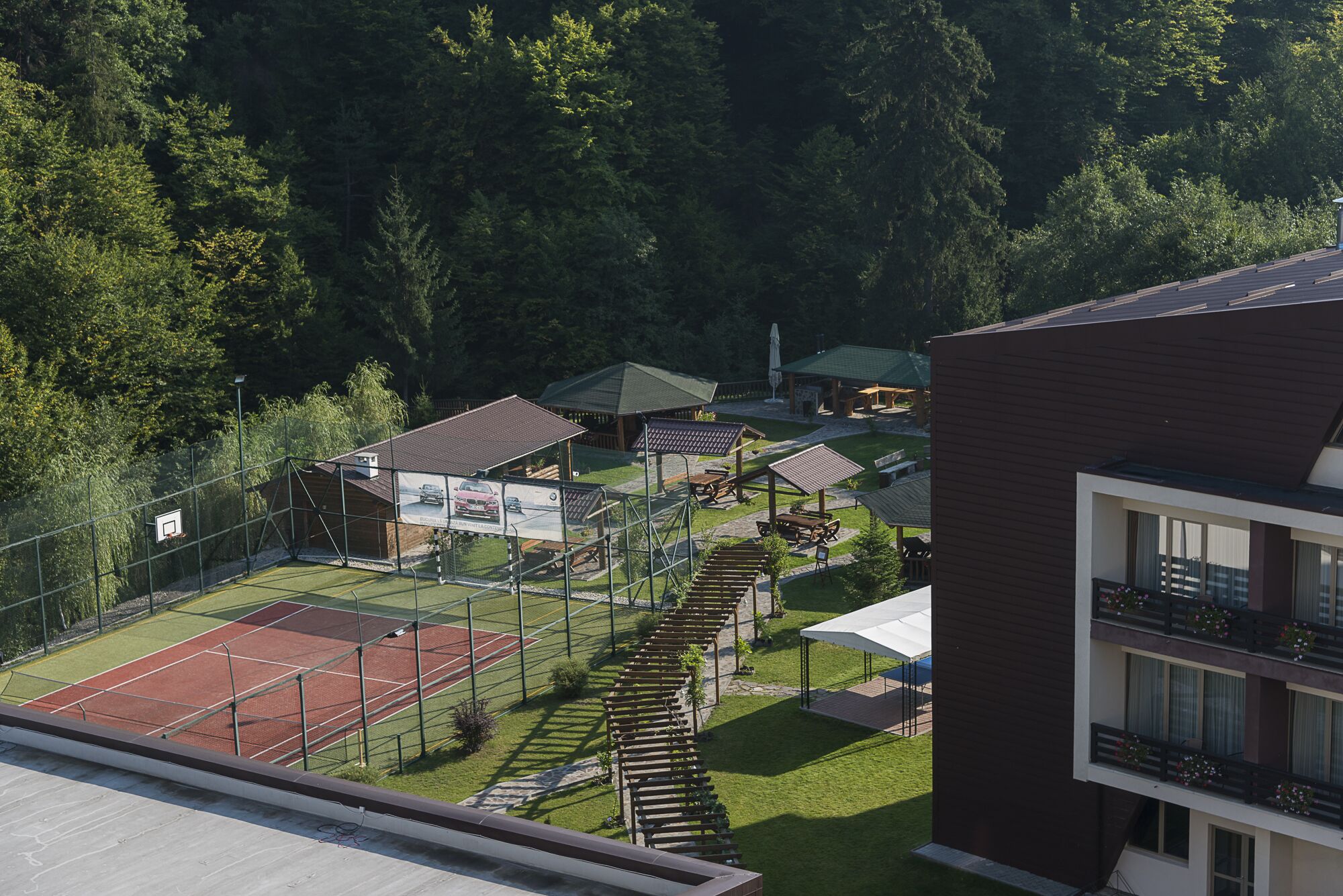 A tennis court surrounded by a fence, with a building and trees in the background.