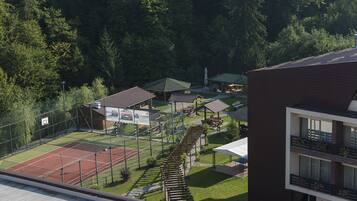 A tennis court surrounded by a fence, with a building and trees in the background.