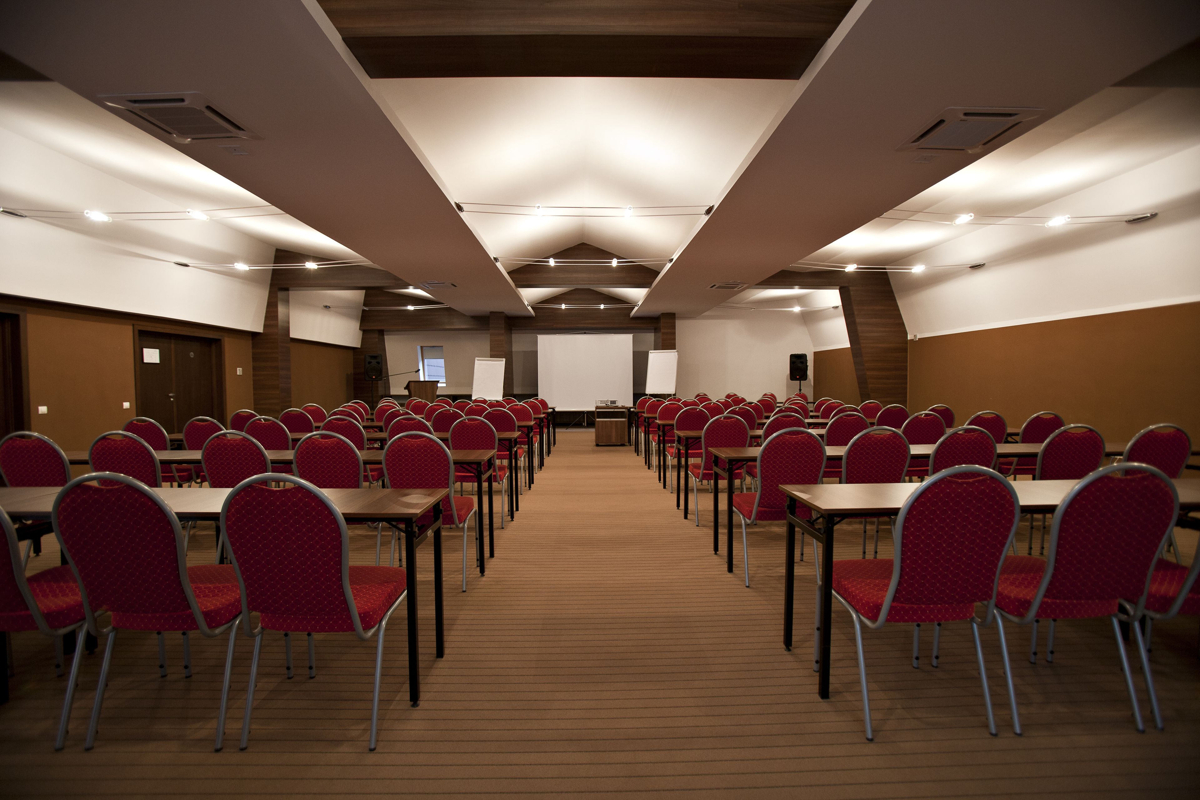 A conference room with rows of tables and chairs, a podium, and a projector screen.