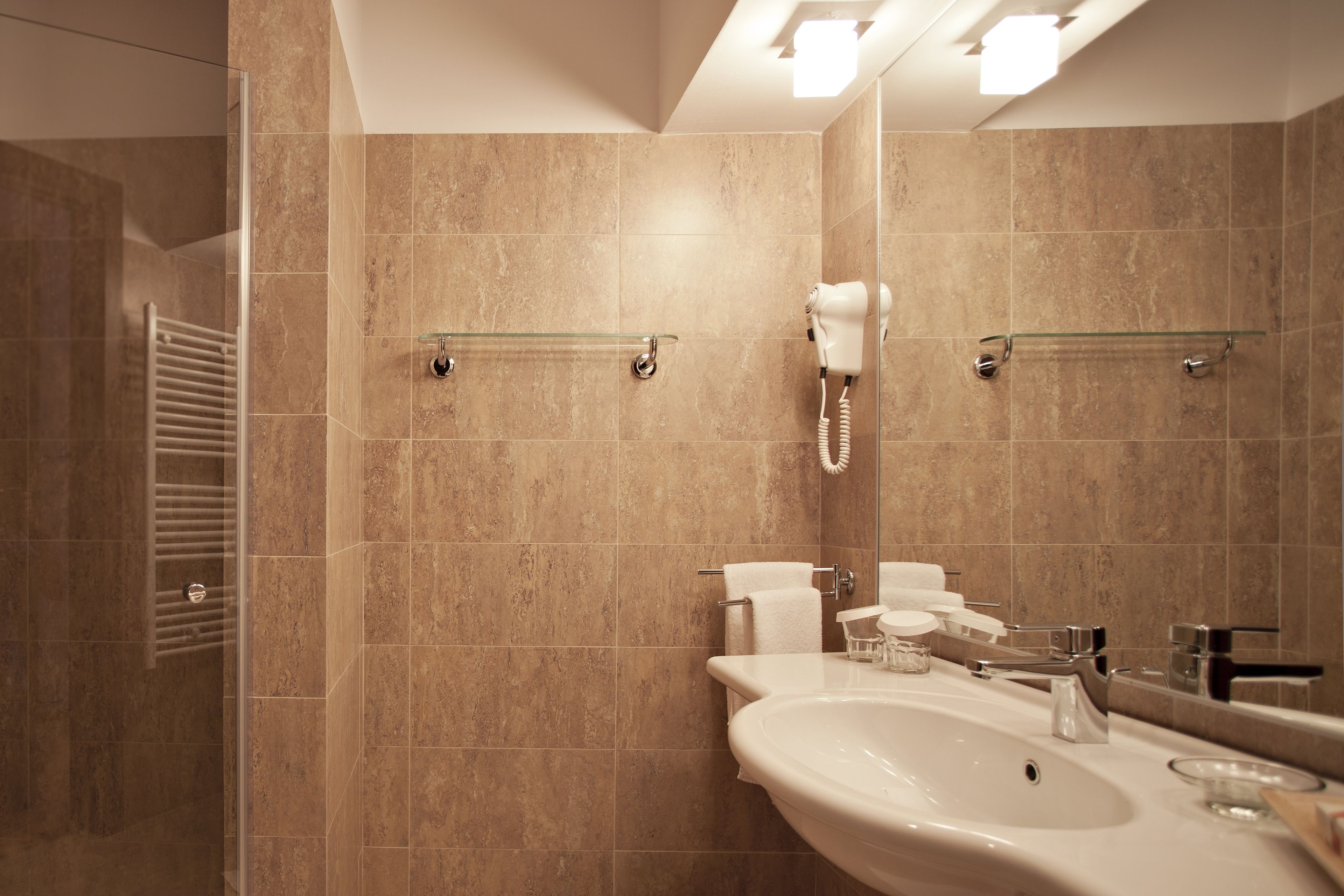A modern bathroom with a large sink, a mirror, a hairdryer, and a glass shower enclosure.