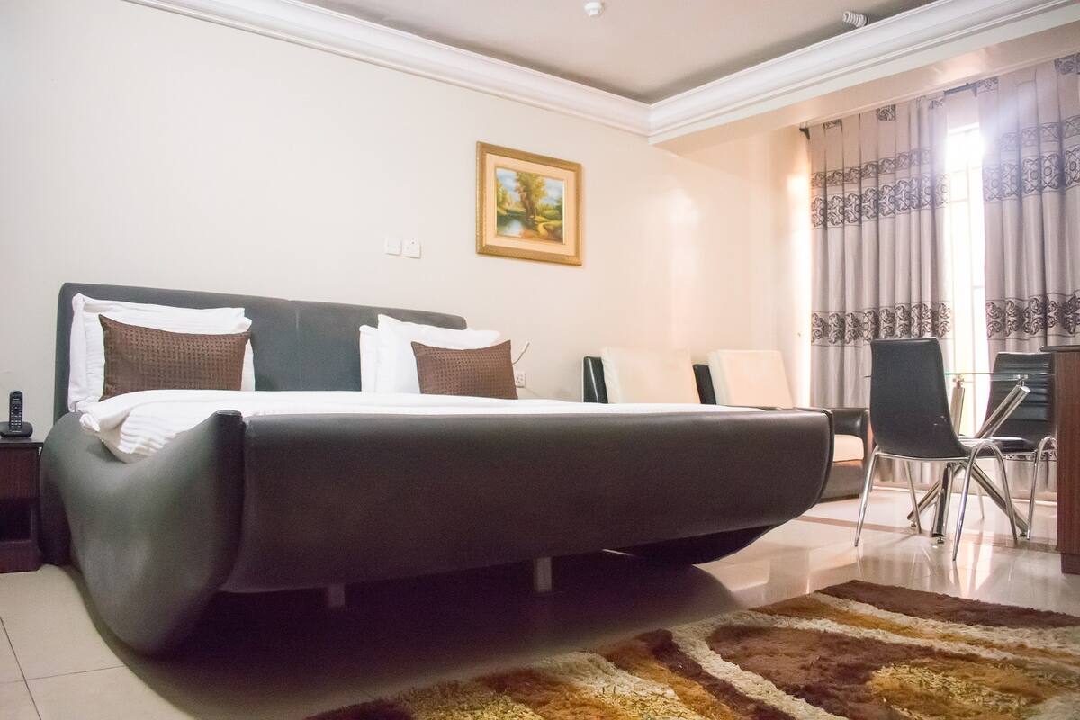 A hotel room with a large bed, a desk, a chair, and a painting on the wall.