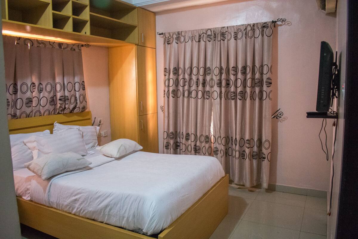 A bedroom with a wooden bed, a wardrobe, a television, and patterned curtains.