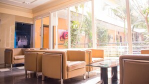 A lobby with beige leather sofas, a glass coffee table, and large windows offering a view of palm trees and a building outside. - Primal Hotel (Lagos)