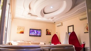 A modern living room with a television, red chairs, and a ceiling with a unique design. - Primal Hotel (Lagos)