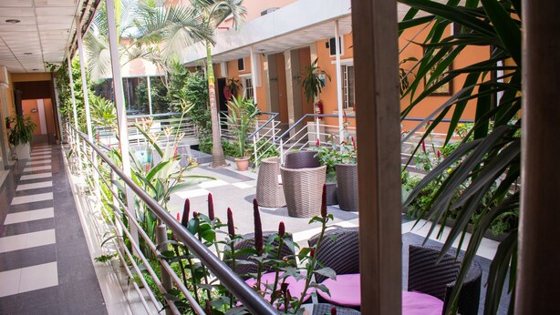 A covered outdoor area with a checkered floor, wicker furniture, and potted plants. - Primal Hotel (Lagos)