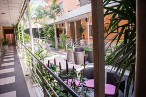Un espacio al aire libre techado con piso a cuadros, muebles de mimbre y plantas en macetas.