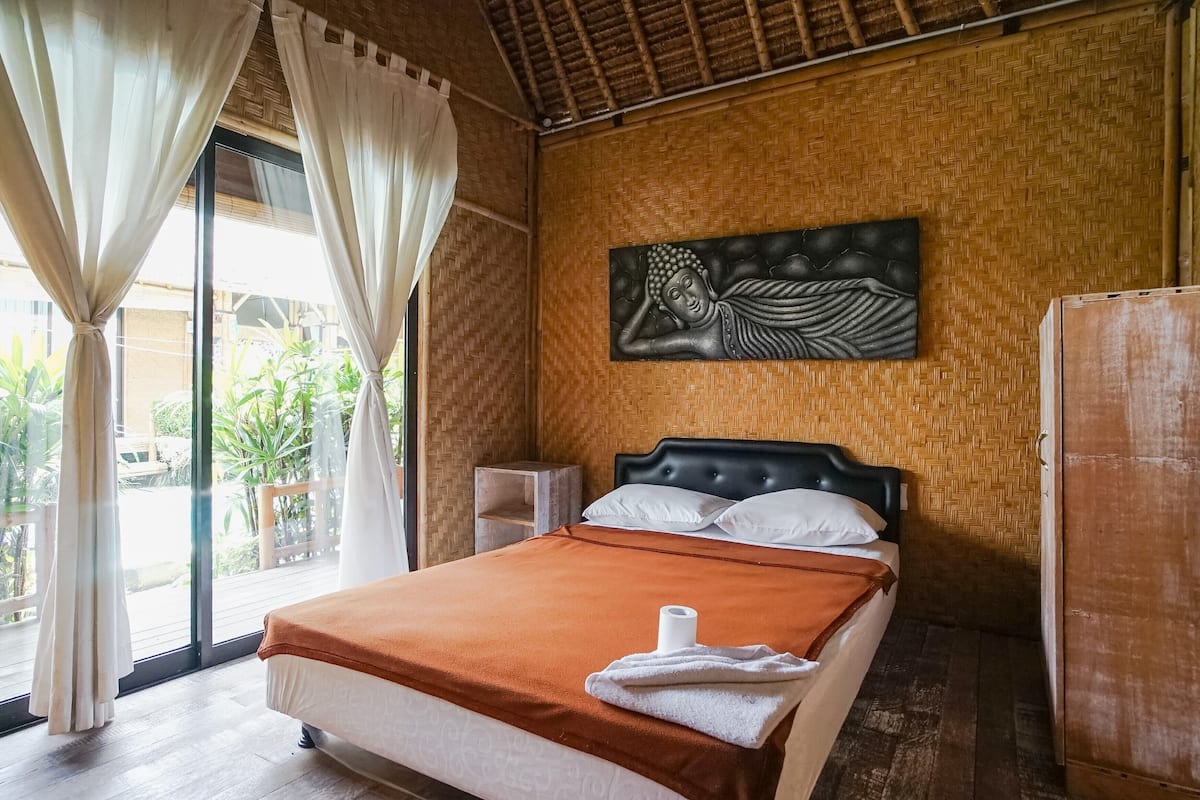 A bedroom with a bed, a headboard, a wall-mounted artwork, a wooden cabinet, and a window with curtains.