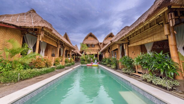 A pool area with thatched-roof structures on either side, surrounded by greenery. - Moon Bamboo (Pererenan)