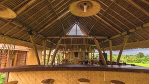 A thatched-roof structure with a central open space, possibly a bar or communal area, surrounded by wooden walls and furniture. - Moon Bamboo (Pererenan)