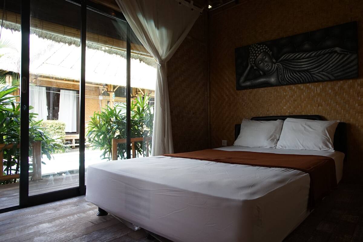 A bedroom with a large bed, a view of the outdoors, and a wall-mounted artwork.