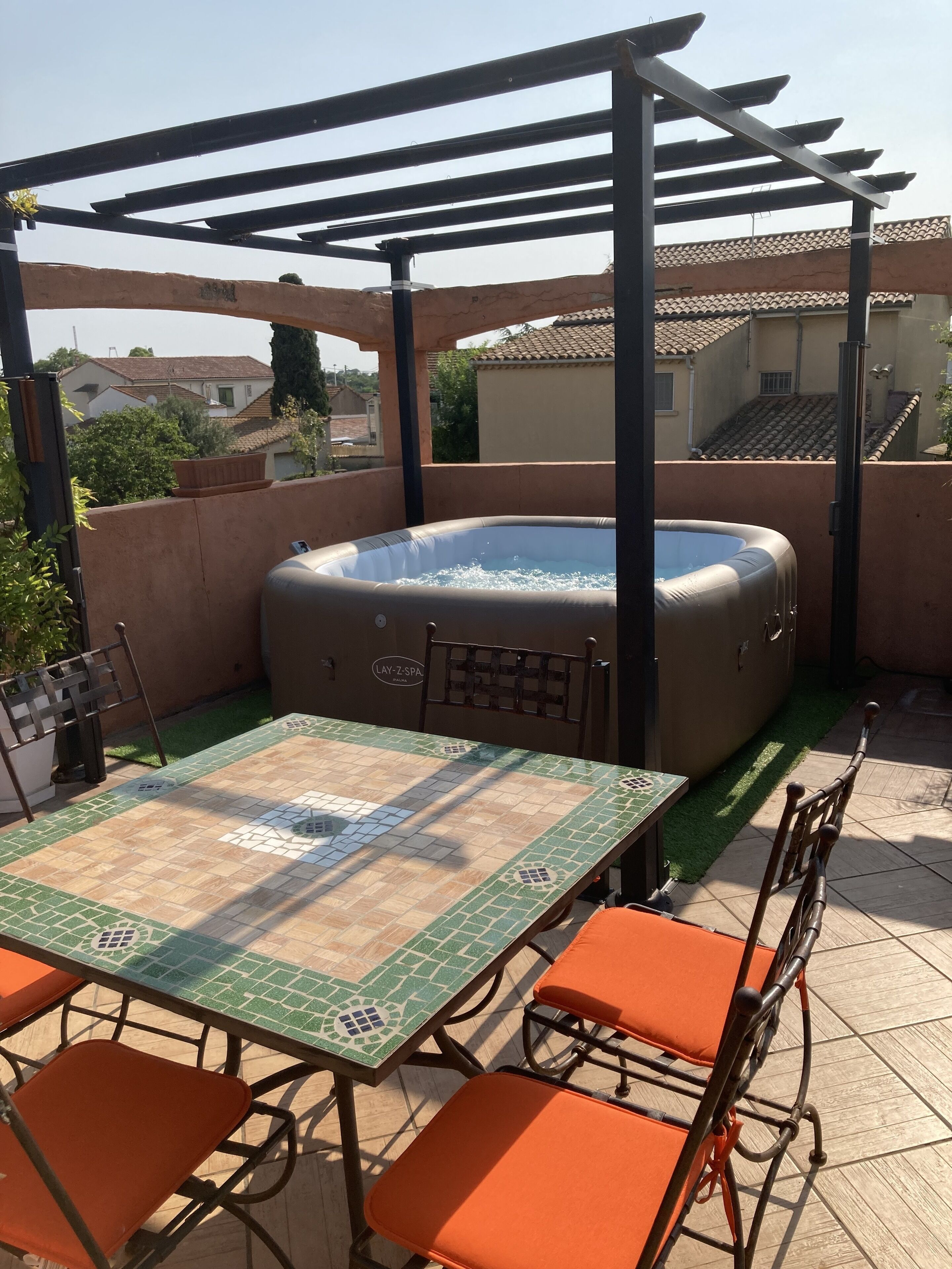 Una terraza en la azotea con un jacuzzi, una mesa de baldosas y sillas naranjas.