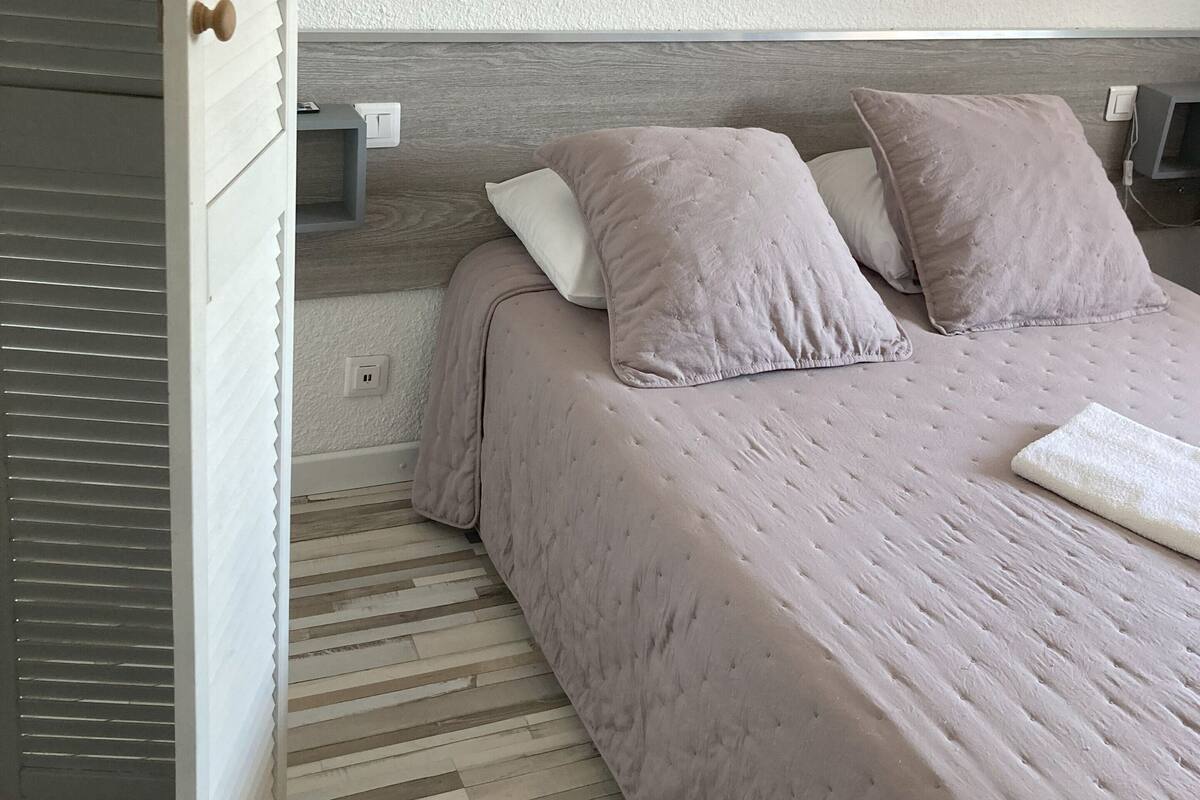 A neatly made bed with a light-colored duvet and pillows, a wooden headboard, and two bedside tables with lamps.