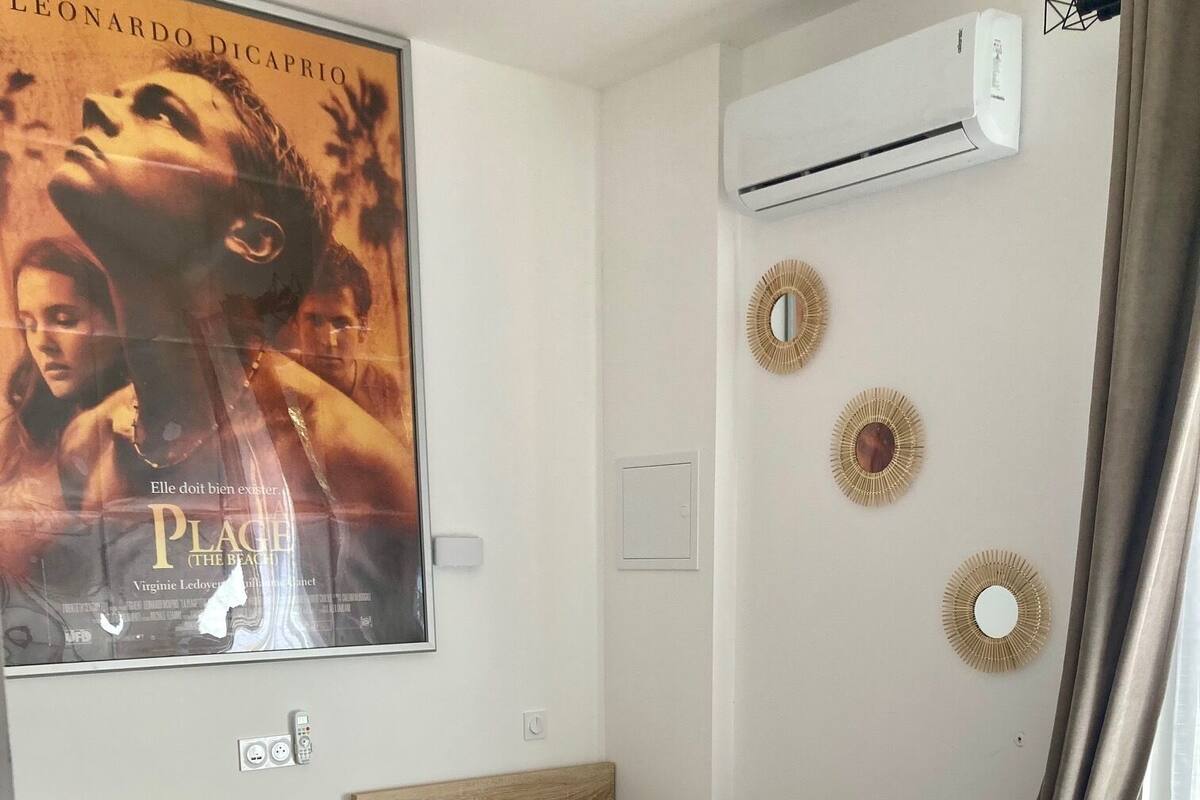 A hotel room with two beds, a poster on the wall, an air conditioner, and a mirror.