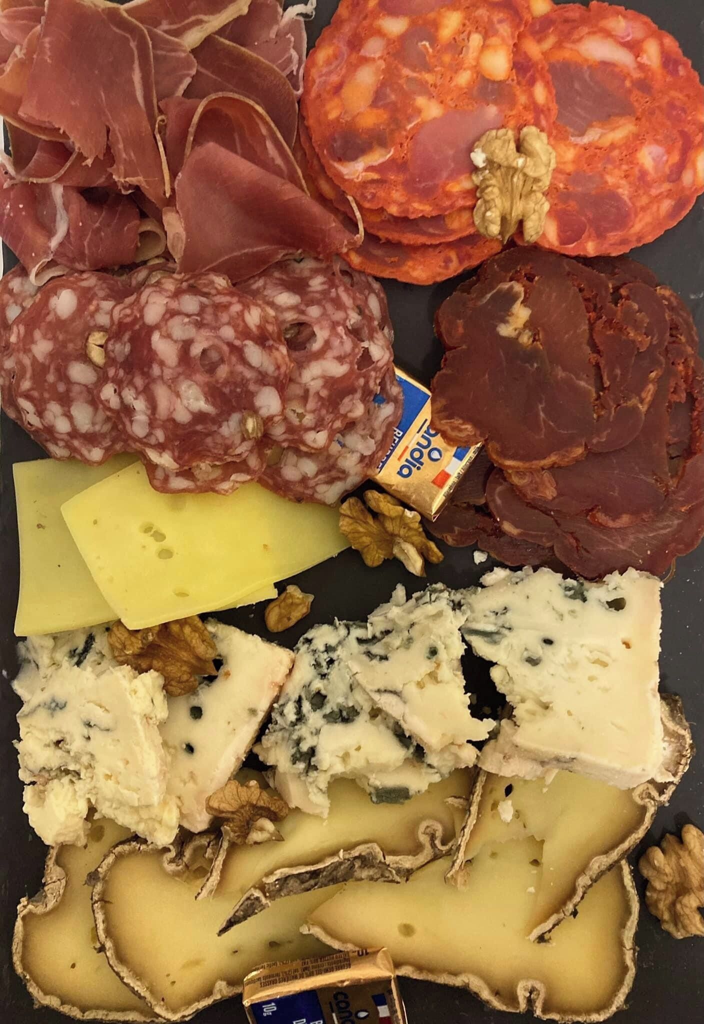 A variety of cured meats, cheeses, and walnuts arranged on a black surface.