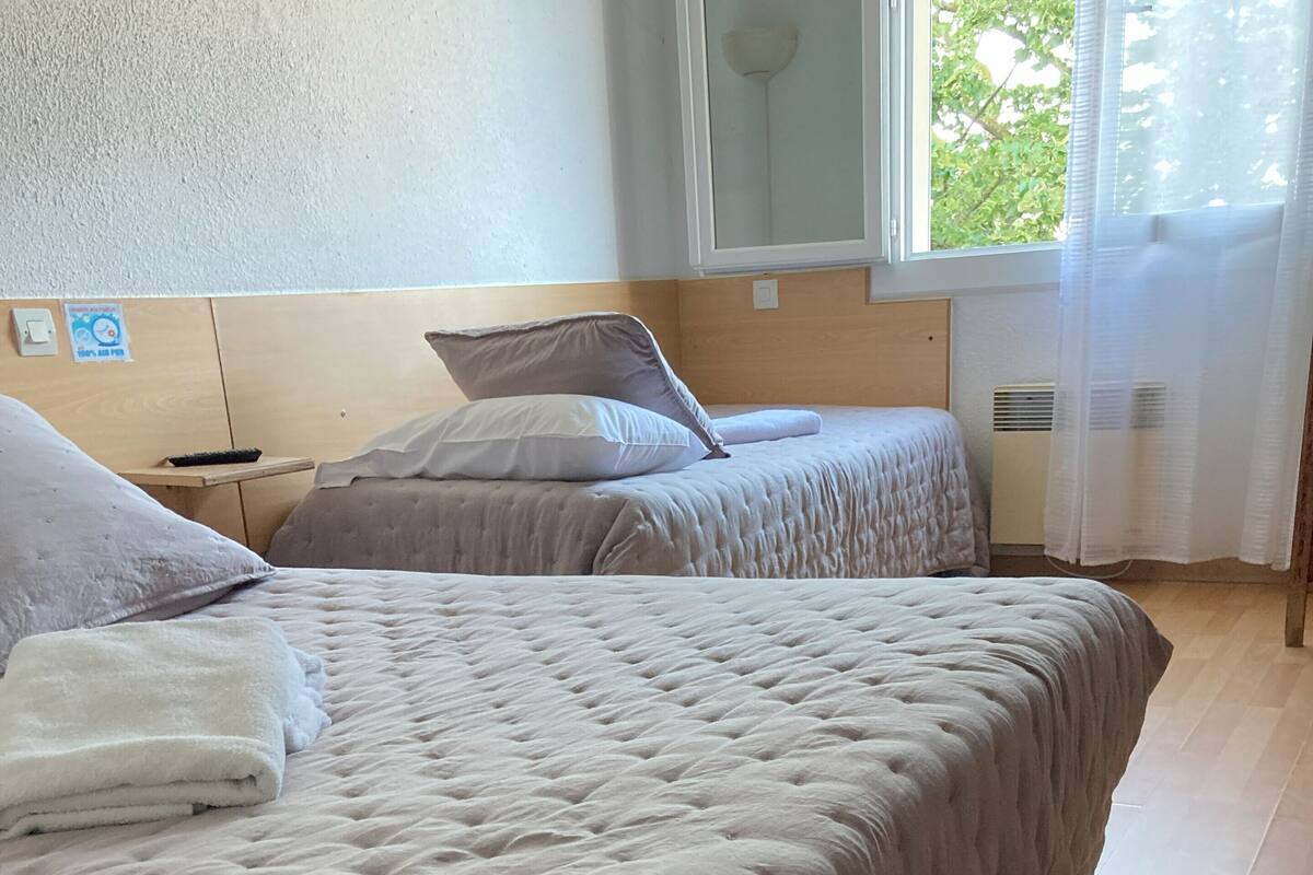 A hotel room with two beds, a wooden headboard, a window with a view of trees, and a tiled floor.