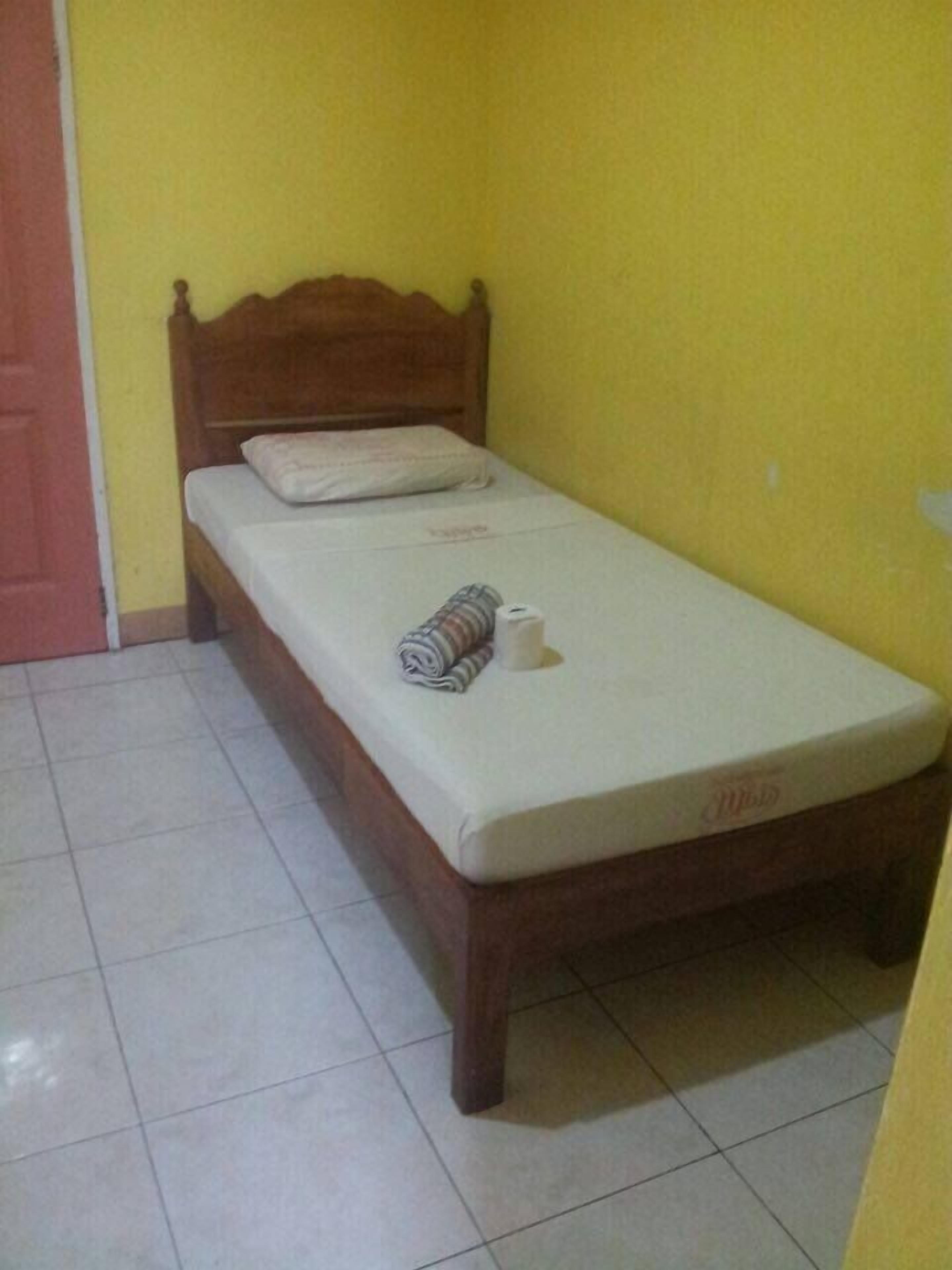 Uma cama de solteiro com cabeceira de madeira em um quarto com paredes amarelas e piso de azulejos brancos.