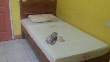 Uma cama de solteiro com cabeceira de madeira em um quarto com paredes amarelas e piso de azulejos brancos.