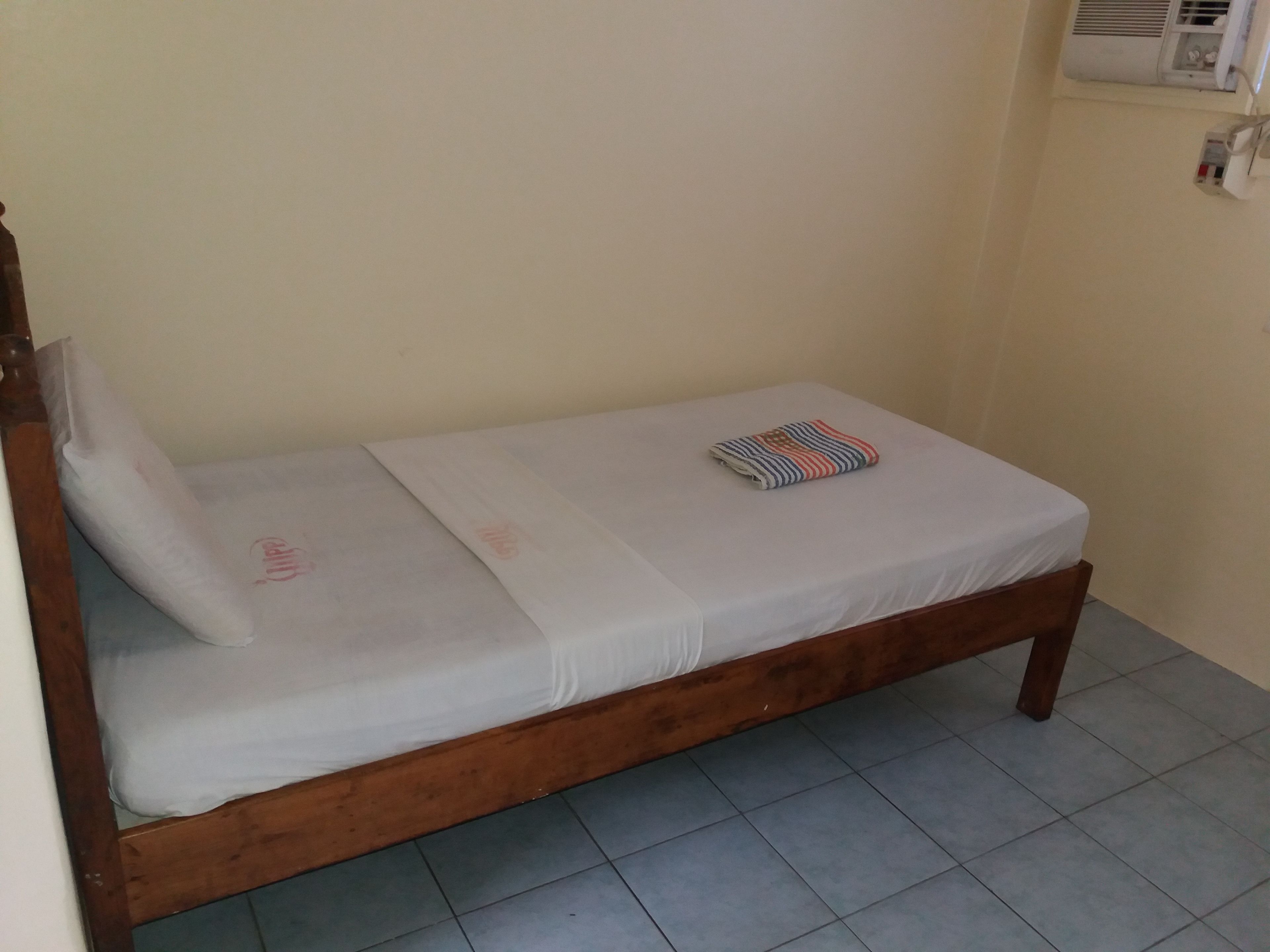 Uma cama de solteiro com estrutura de madeira, colchão branco e um cobertor dobrado.