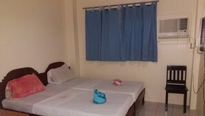 Een kamer met een bed, een stoel, een raam met gordijnen en een airconditioning.